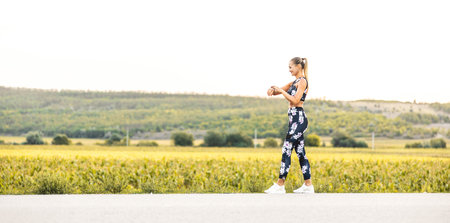 The athlete watches cardio, fitness in the city. A woman looks at sports and counts calories during training. Exercise coach on the street, healthy lifestyle.の写真素材
