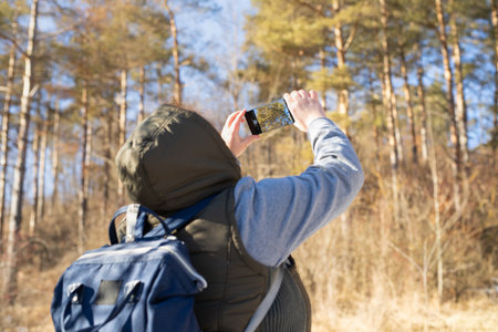 Back view photo of a female hiker with a backpack taking a photo with her mobile phone of the beautiful nature around her.の写真素材