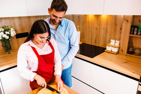 Loving young couple cutting vegetables together at kitchen counter. Young man and woman in love cooking food together at home.の写真素材