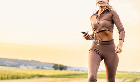 Fitness, sport and healthy lifestyle concept - smiling woman with earphones wearing armband for smartphone, jogging at summer park and listening to musicの写真素材