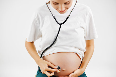 Beautiful Pregnant woman in white shirt listening through a stethoscope that makes her a child and looked at her belly on the white background.の写真素材