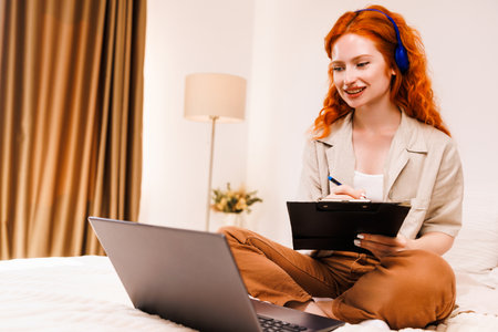 Young woman sitting on the bed and working on a computer and make some notes.の写真素材