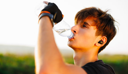 Man drinking water after running workout at beach. Thirsty healthy male with fit body drinking water.の写真素材