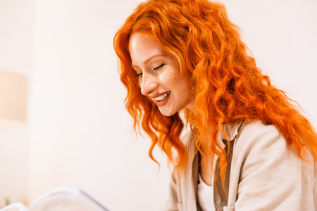 Close up portrait of an attractive smiling happy young woman with long curly red hair standing isolated over home background.の写真素材