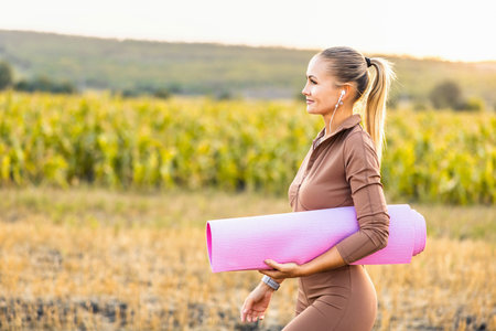 Beautiful happy woman with a pink yoga mat outdoors walks forward while listening to music in headphones.の写真素材