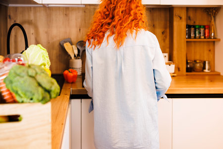 Photo of pretty caucasian woman holding cooking ladle spoon while eating soup with fresh vegetables in kitchen at homeの写真素材