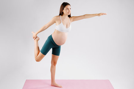Portrait of dark haired pregnant woman doing aerobics in sports studio on pink yoga mat. Lateral vision. Healthy sportの写真素材