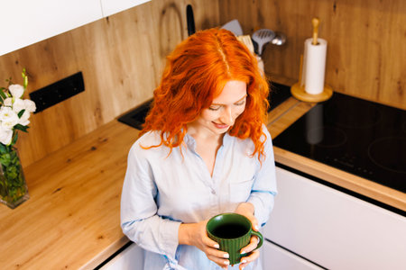 Happy dreamy senior blonde lady enjoying good morning, drinking hot coffee at home, resting on...
