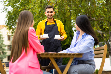 Waiter with protective medical mask and gloves serving guest with coffee at an outdoor bar caffee or restaurant new normal concept reopening after quarantineの写真素材