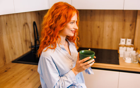 Young happy woman sitting in the balcony and having breakfast, she is drinking orange juice and smiling at cameraの写真素材