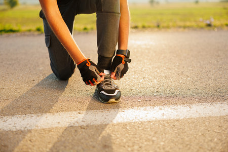 Cropped image of an athlete runner tying shoelaces, standing on a treadmill of the urban glass city bridge, ready for morning jog. Close-upの写真素材