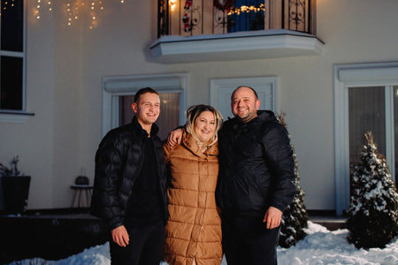Smiling widely family of three persons adult mother, father and their son hugging together with happy mood standing outside on winter holiday night.の写真素材
