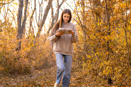 Beautiful woman using map to navigate in autumn forest. Happy tourist trying to find the best way. Active lifestyle, travel concept. . High quality photoの写真素材
