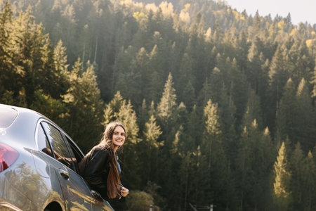 Freedom, travel and a happy woman looking back through the car window. Relaxation and happiness on the road of rural adventure. Travel, outdoor vacation in the mountains.の写真素材