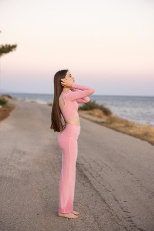 An Elegant Woman in a Beautiful Pink Outfit Standing Gracefully by the Seaside at Sunsetの写真素材