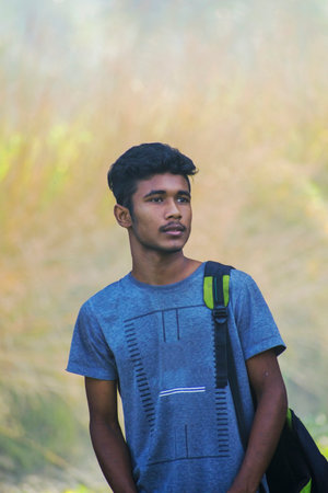 Portrait of a teenager boy with school bag in his back in front of natural outdoor background and lookingの写真素材