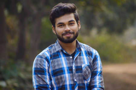 A young boy with blue check shirt looking at the camera with smile in front of natural background in outdoor with a sunny dayの写真素材