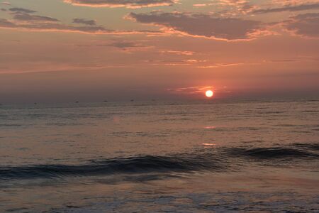 sun setting in a ocean with small waves and beautiful skyの写真素材