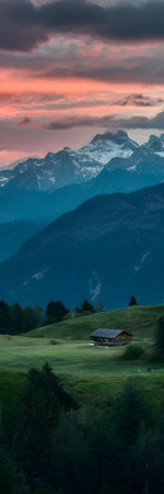 Dramatic sunset over snow-capped mountains and a green valley with a small house. Clear details a...の写真素材