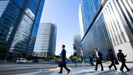 Businessmen crossing a street in a modern city with tall skyscrapers under a clear blue sky.の写真素材
