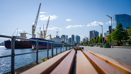 Cargo ships are docked by a waterfront promenade with a modern city skyline in the background.の写真素材