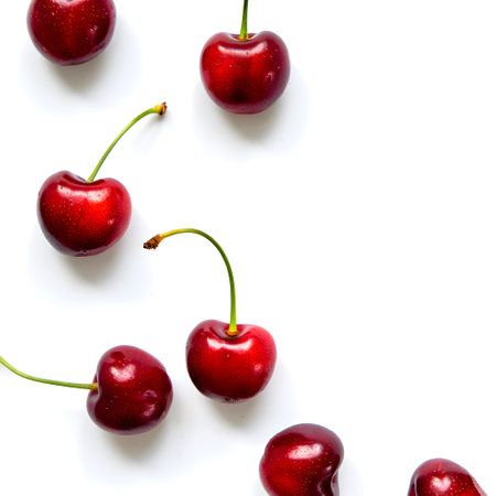 Several ripe red cherries with green stems are scattered on a white background. Clear details and...