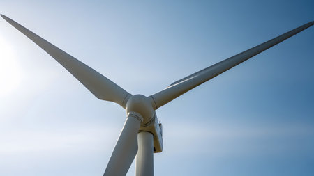 A white wind turbine with three long, angled blades stands prominently against a vast, clear...の写真素材