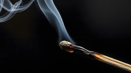 Against showing burning matchstick with orange flame and white smoke against a dark background....