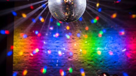 Textured showing disco ball reflects colorful lights onto a textured brick wall creating a...