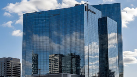A tall glass skyscraper with a blue facade reflects the sky and clouds, showcasing modern urban architecture.の写真素材
