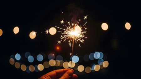 Night showing sparkler held in hand at night with blurred bokeh lights in background.