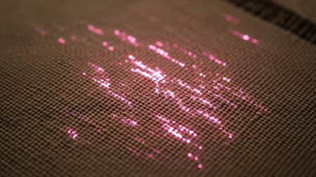Light showing pink light streaks on brown woven fabric texture with shallow depth of field.