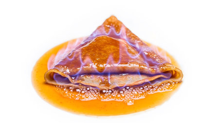 Blue showing close-up of a flaming crepe suzette with bubbling orange sauce and blue flames....