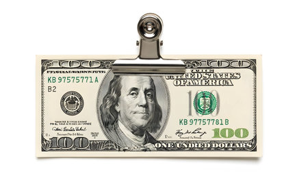 A silver bulldog clip firmly holds a one hundred dollar bill against a stark white background.