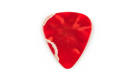 Guitar pick with red, white, and beige chipped edges and visible scratches on a white background.