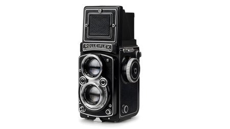 A vintage black Rolleiflex twin lens reflex camera with silver detailing stands against a clean...