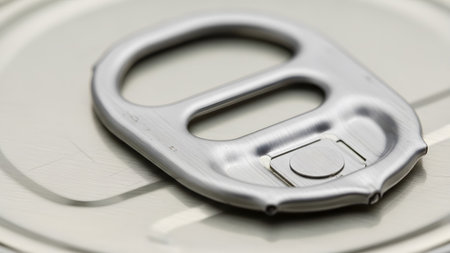 Detailed macro view of a silver pull tab on a textured metallic beverage can lid, showing fine...