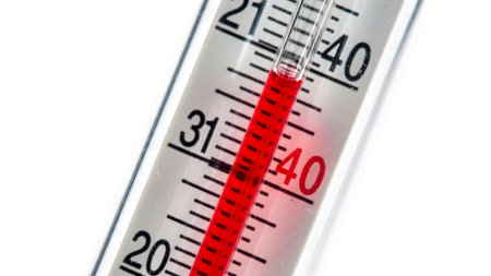 Close showing close up of a thermometer showing red liquid rising on a white background with...