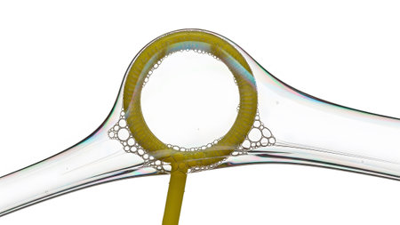 A close-up view of a yellow bubble wand forming iridescent soap bubbles and a thin soap with...