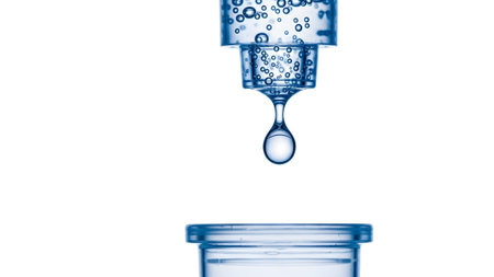 A single clear water droplet suspended mid-air as it falls from a transparent dispenser nozzle.
