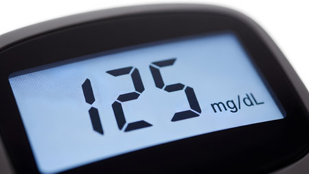 Background showing digital display of a glucose meter showing a reading of 125 mg/dl on a white...