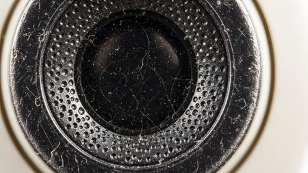 An extreme close-up of a black earbud speaker grille showing dust, scratches, and a perforated...の写真素材