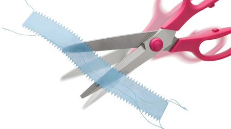 Motion showing pink handled scissors in motion cutting a light blue fabric strip with a serrated...