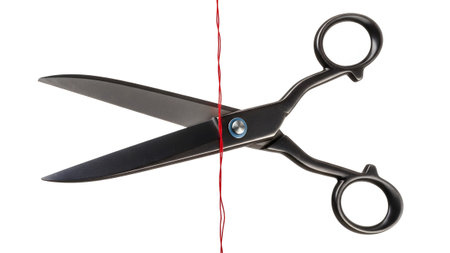 Sharp metal scissors in the process of cutting a thin red thread against a clean white background.