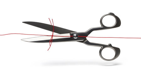A pair of sharp steel scissors with open blades is positioned to cut a thin red thread on a...