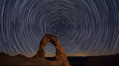 A long exposure shot of star trails circling above the iconic sandstone Delicate Arch at night.