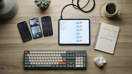 A top-down view of a wooden desk featuring a tablet with data charts, smartphones, and a keyboard.