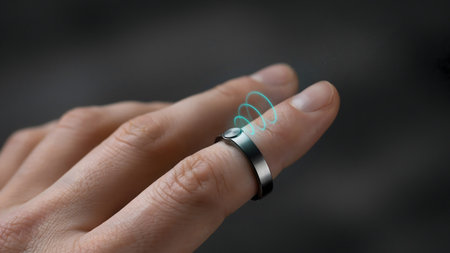A person wears a smart ring on their finger with a glowing wireless signal interface visible above.