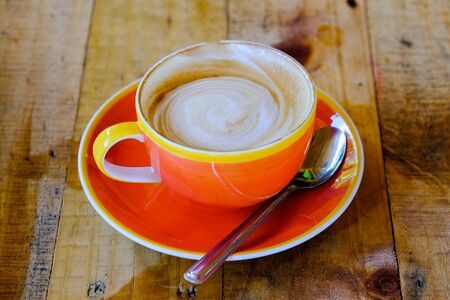 Top view of cappuccino coffee with art dress up in orange cup on polished wooden table surfaceの写真素材