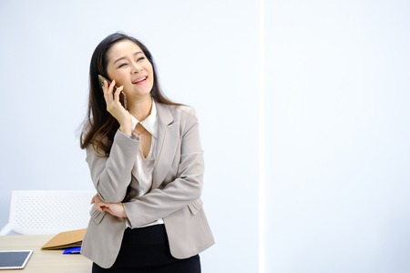 businesswoman talking on mobile phone while standing by window in office.の写真素材